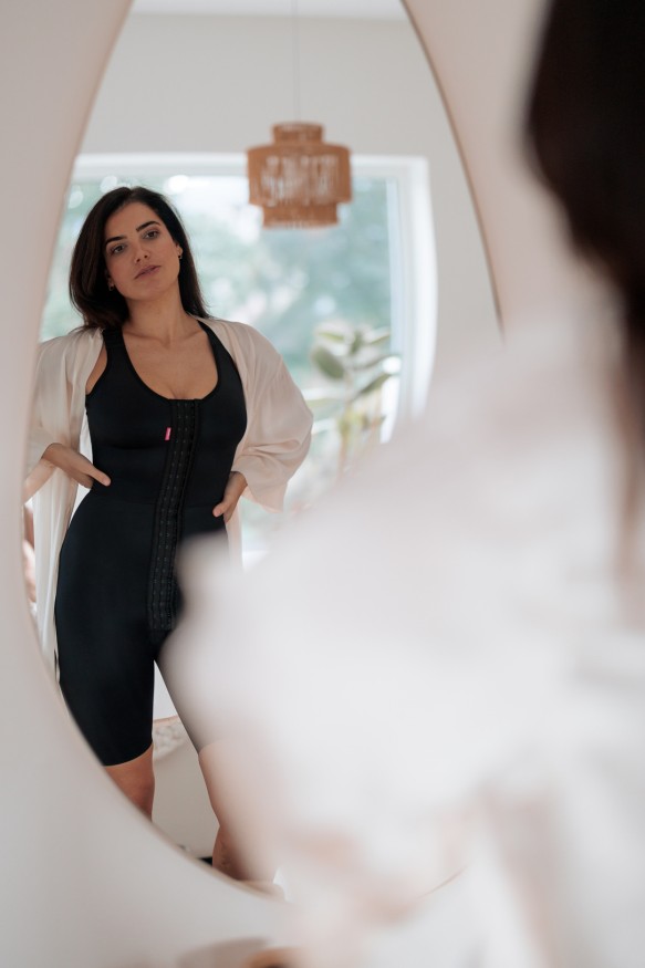 Frau im Kompressionsbody schaut sich im Spiegel an