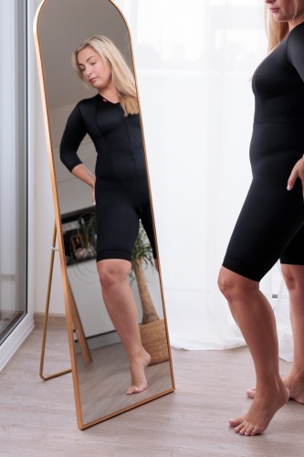 Frau steht vor einem Spiegel und trägt einen Kompressionsbody von LIPOELASTIC 