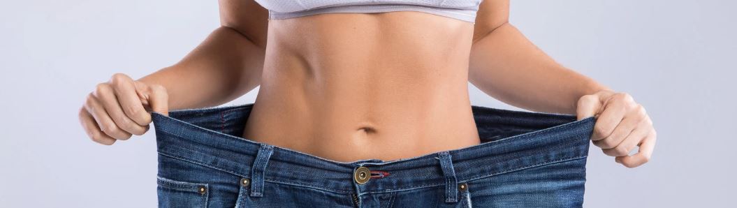 Frau mit flachem Bauch hat eine sehr weite Hose an, die ihr nach der Magen-OP zu groß ist.